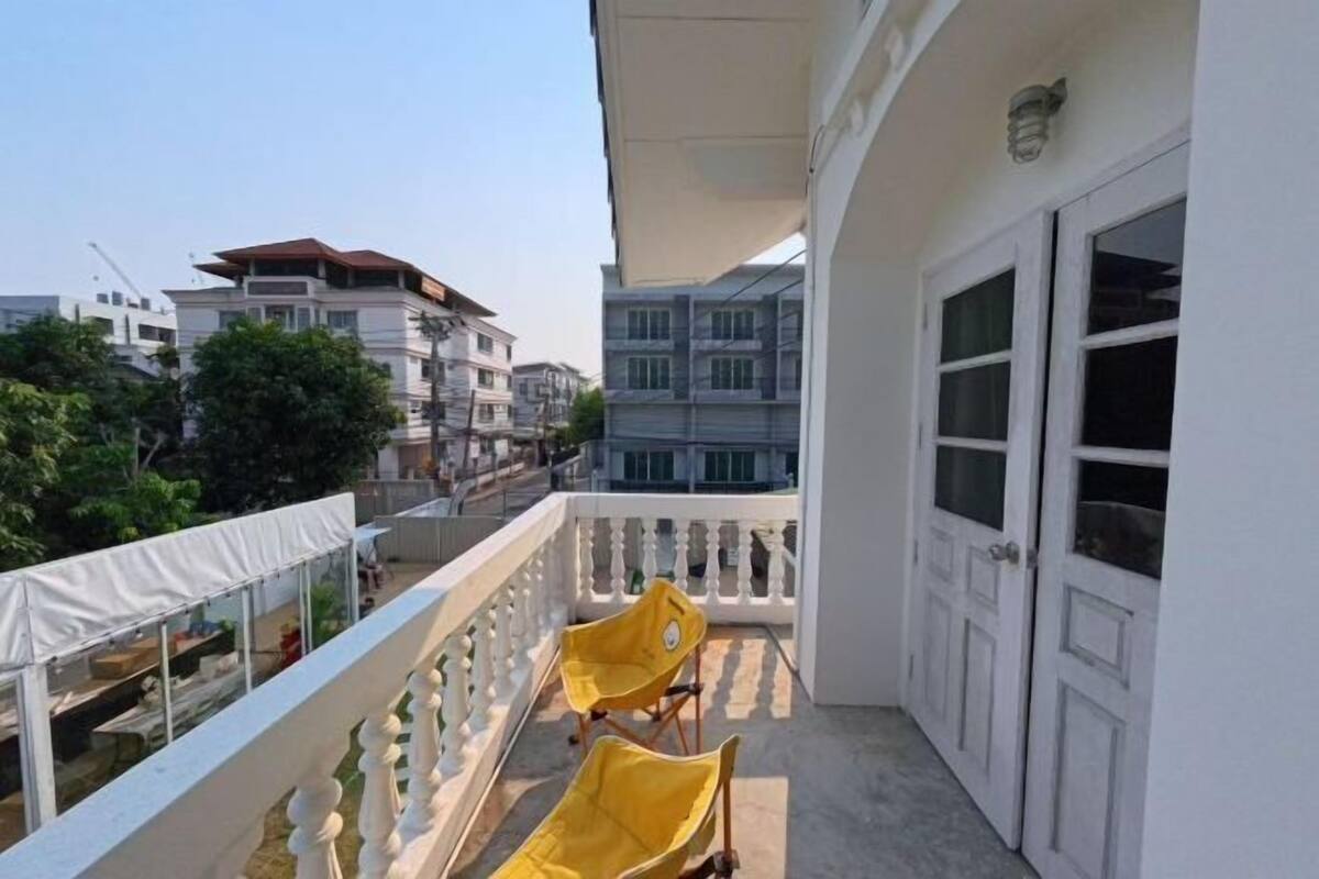 A balcony with a white railing, two yellow chairs, and a white door.