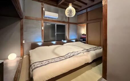 A traditional Japanese-style room with tatami flooring, a large bed with a patterned blanket, a hanging light fixture, and a sliding door.