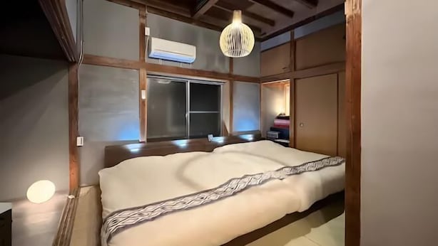 A traditional Japanese-style room with tatami flooring, a large bed with a patterned blanket, a hanging light fixture, and a sliding door.