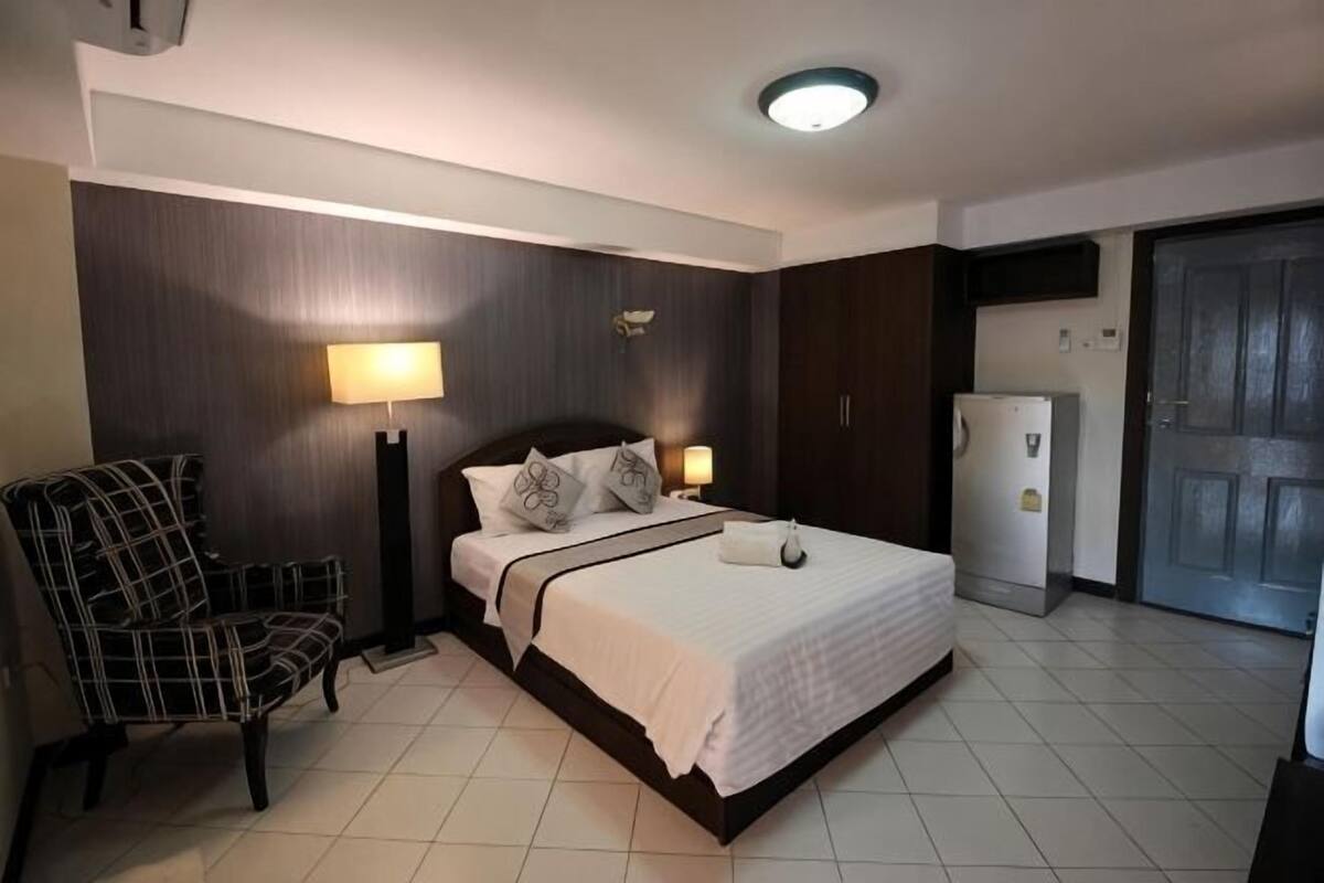Een hotelkamer met een bed, een stoel, een bureau, een lamp en een koelkast.