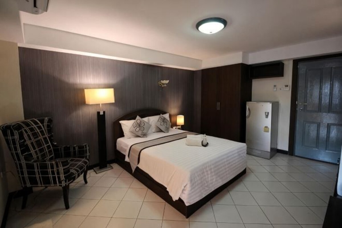 Een hotelkamer met een bed, een stoel, een bureau, een lamp en een koelkast.