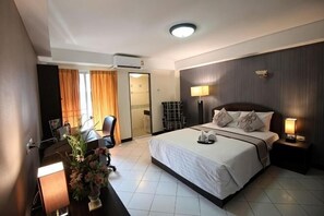 Habitación de hotel con una cama grande, un escritorio, una silla, una lámpara y un televisor montado en la pared.