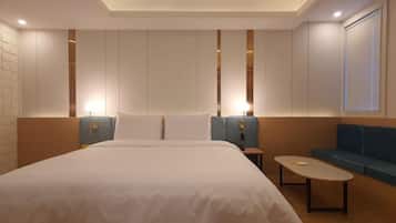 A modern hotel room with a large bed, a small table, a sofa, and a wall-mounted TV.