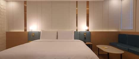 Una habitación de hotel moderna con una cama grande, una mesita, un sofá y un televisor montado en la pared.