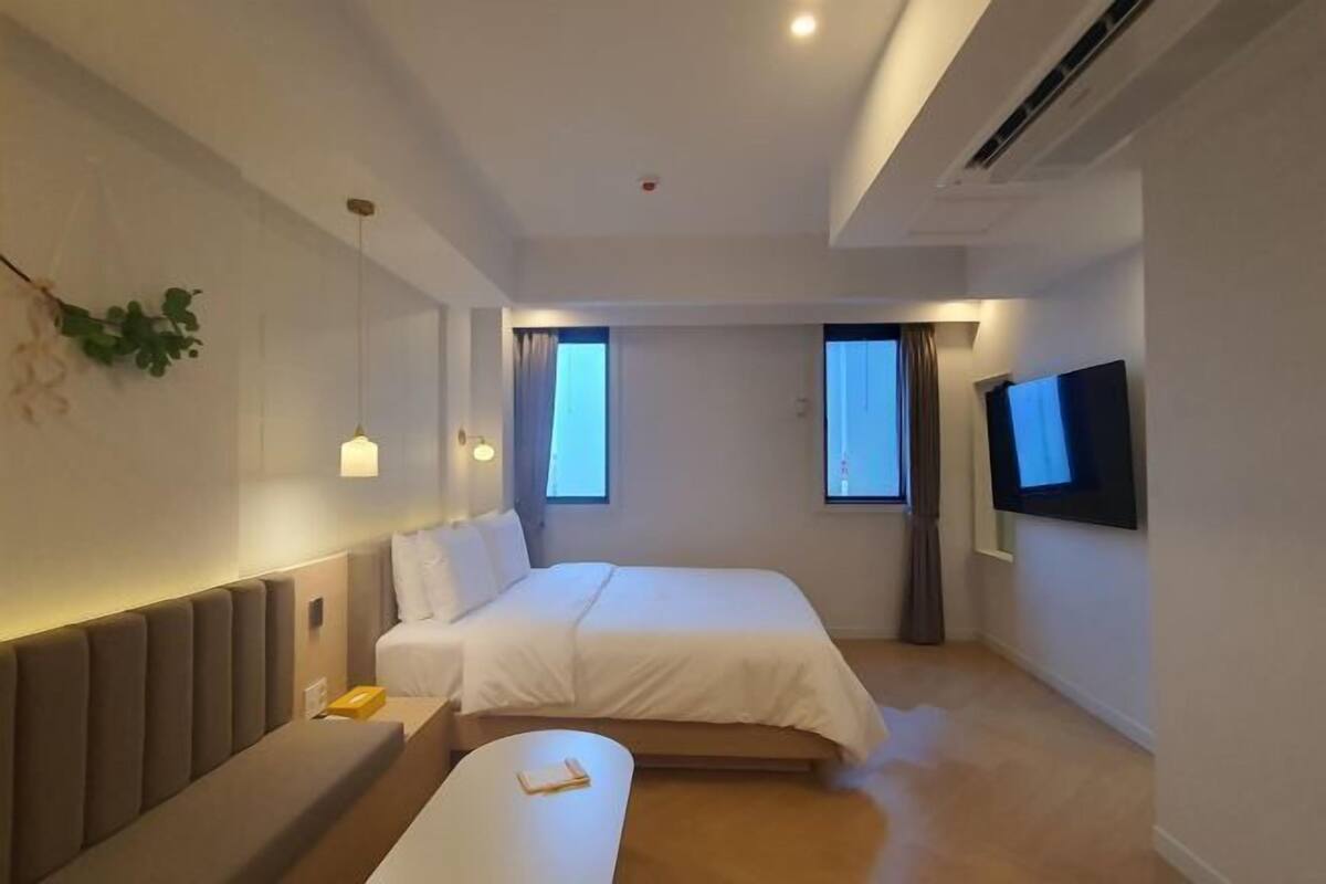 A modern hotel room with a bed, bedside table, and a flat-screen TV mounted on the wall.