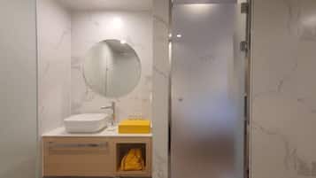 A bathroom with a marble wall, a round mirror, a white sink, a yellow soap dispenser, and a towel rack.