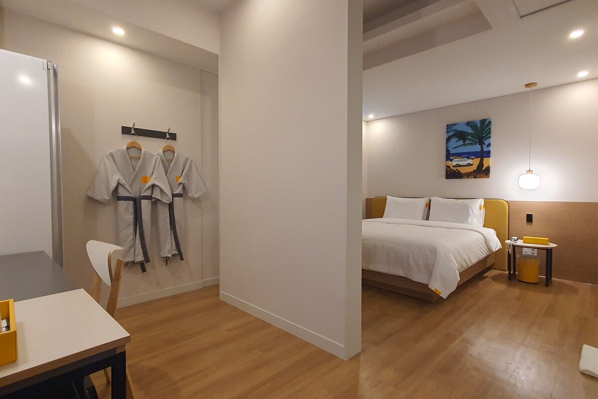 Una habitación de hotel con cama, mesita de noche, lámpara y un cuadro en la pared.