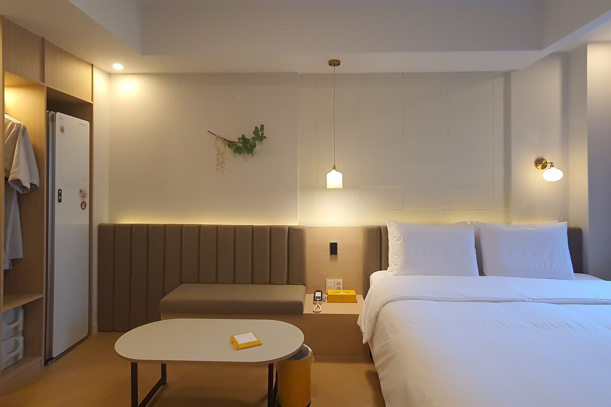 Una habitación de hotel con cama, mesita de noche y una zona de estar con mesa y banco.