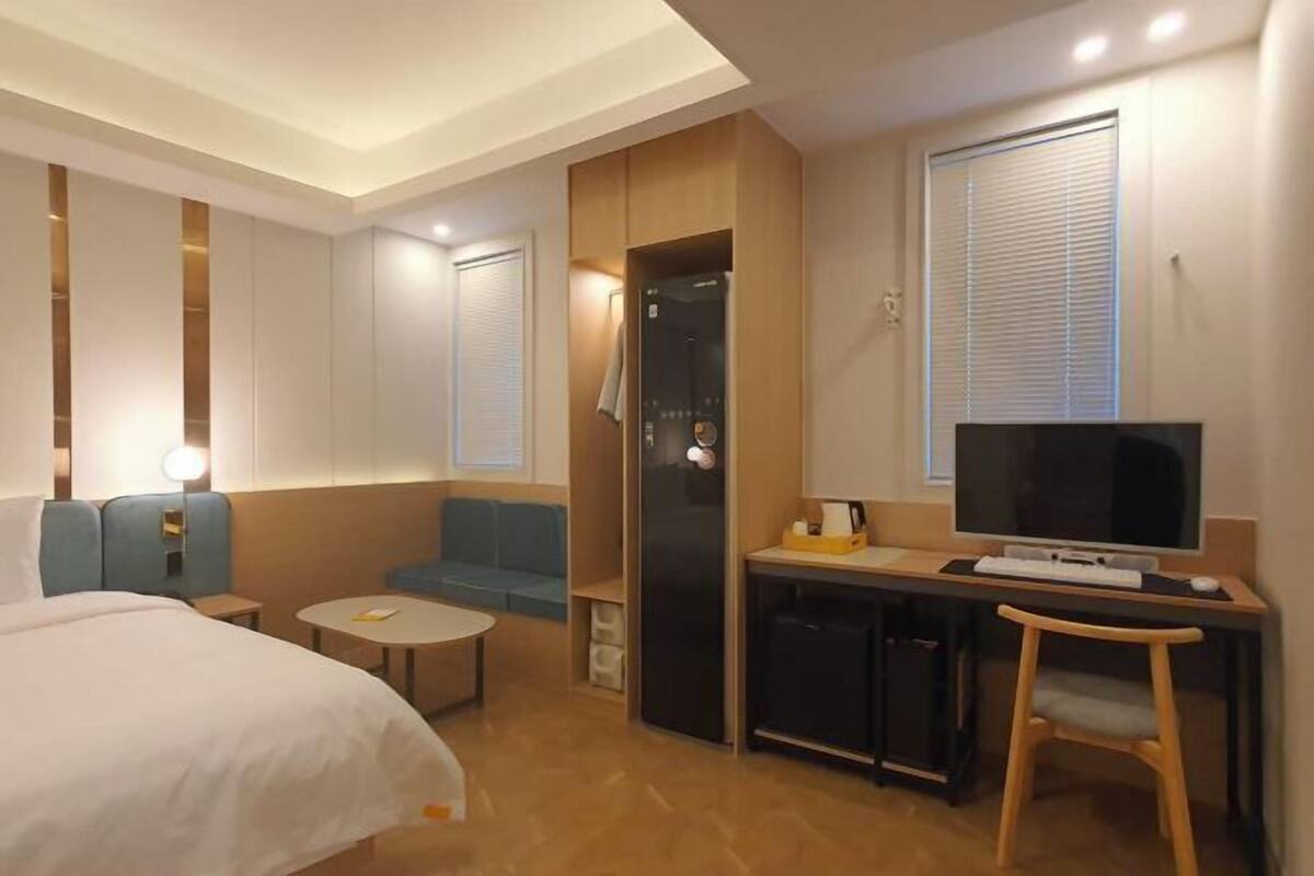 A hotel room with a bed, a desk with a computer, a TV, a small table, and a seating area.
