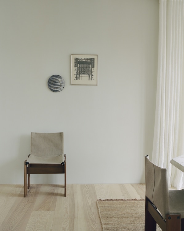 Una habitación con una silla de madera, un tapete, un cuadro enmarco y una cortina.