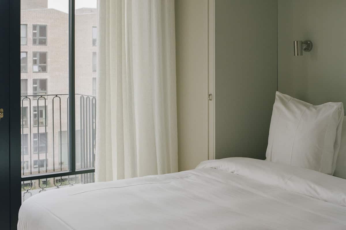 Habitación de hotel con una cama grande, un armario y un balcón con vistas a edificios.