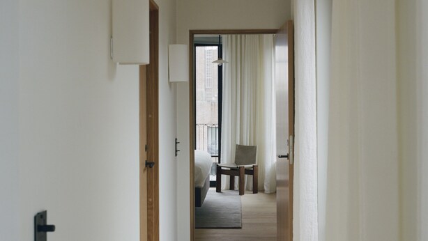 Ein Flur, der in ein Schlafzimmer mit Bett, Stuhl und Fenster führt.