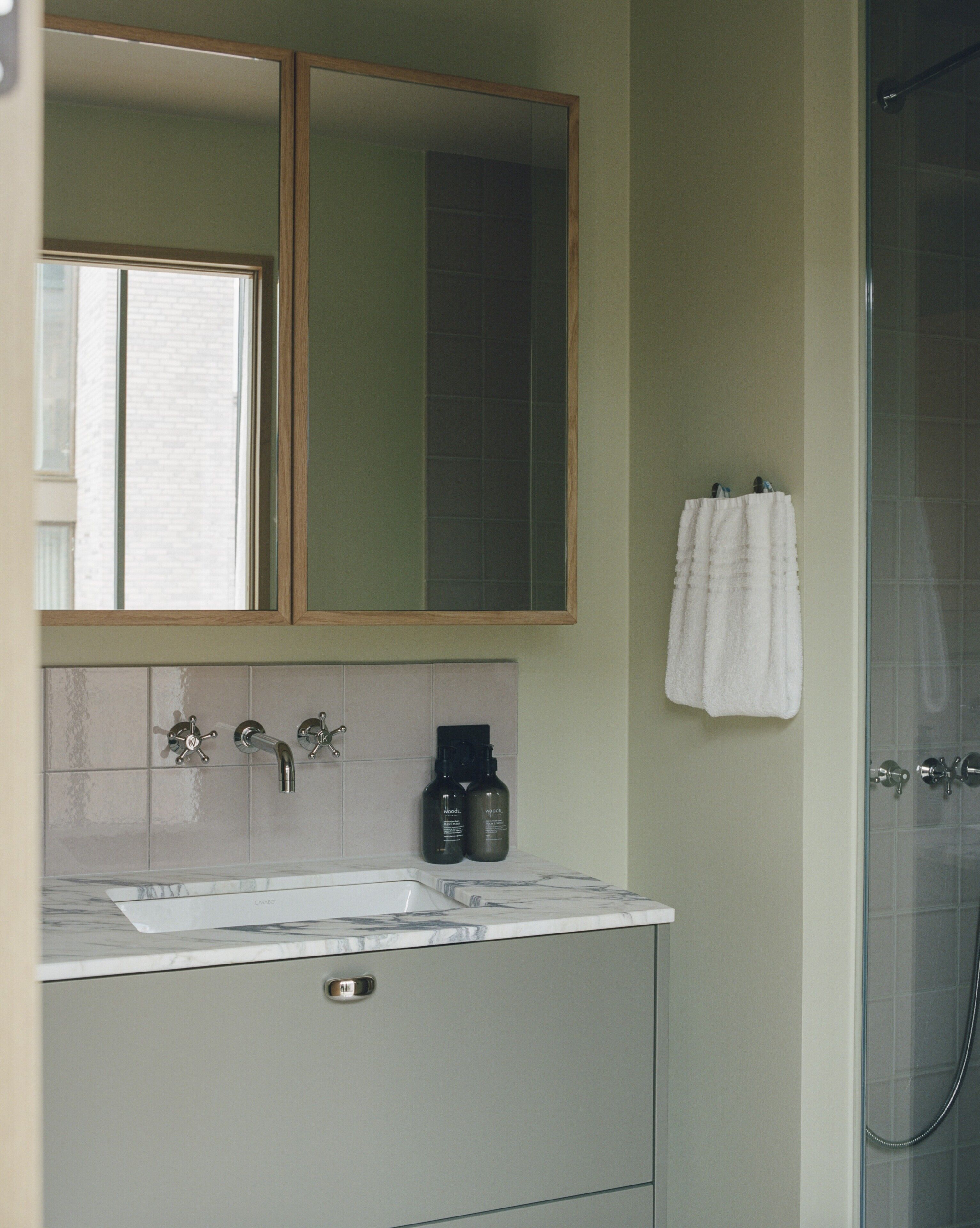 A bathroom with a mirror, two sinks, a towel rack, and a shower.
