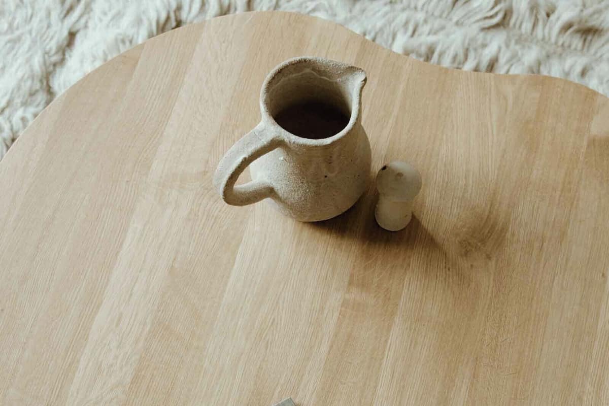 Una mesa de madera con una jarra de cerámica y un libro titulado 'THE GRAMMAR'.