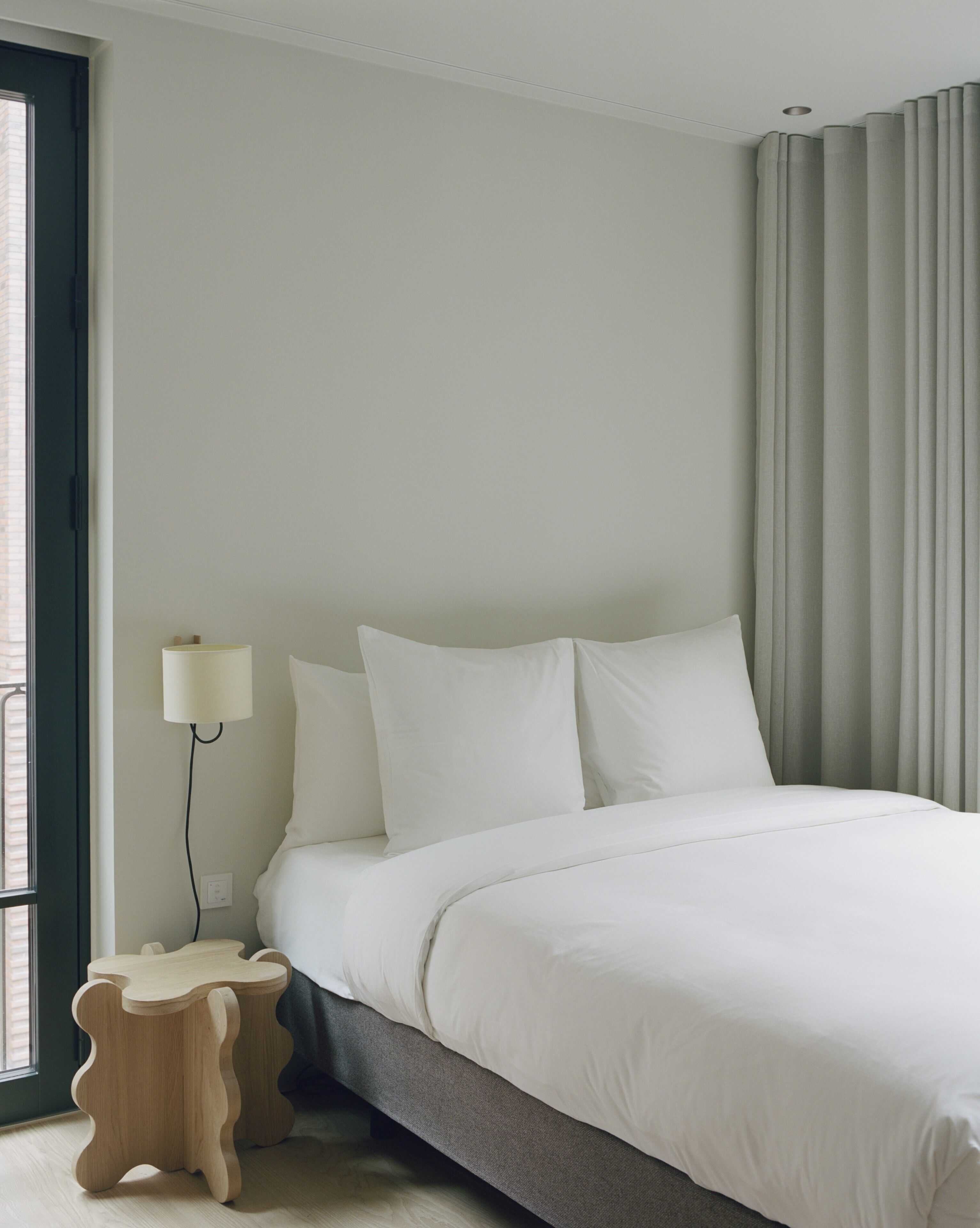 A bedroom with a bed, a bedside table, a lamp, and a window with curtains.