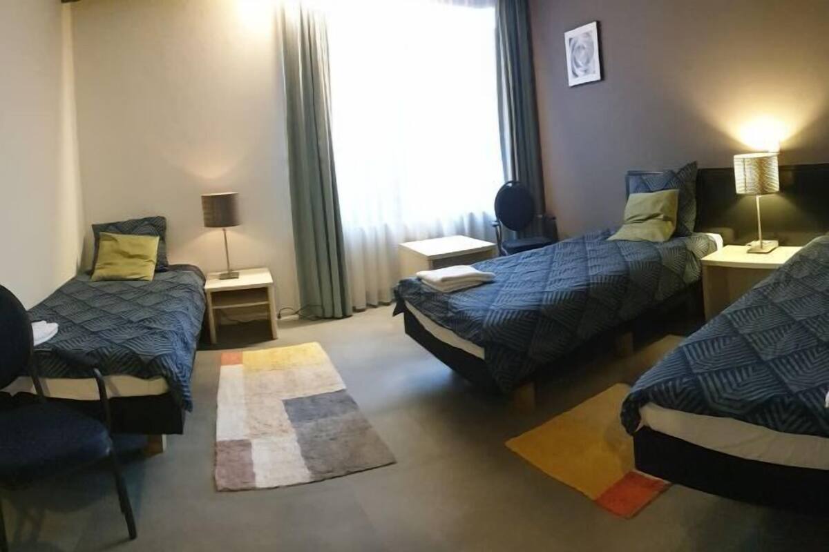 Une chambre d’hôtel avec deux lits, un bureau, une chaise, une lampe et une fenêtre avec des rideaux.