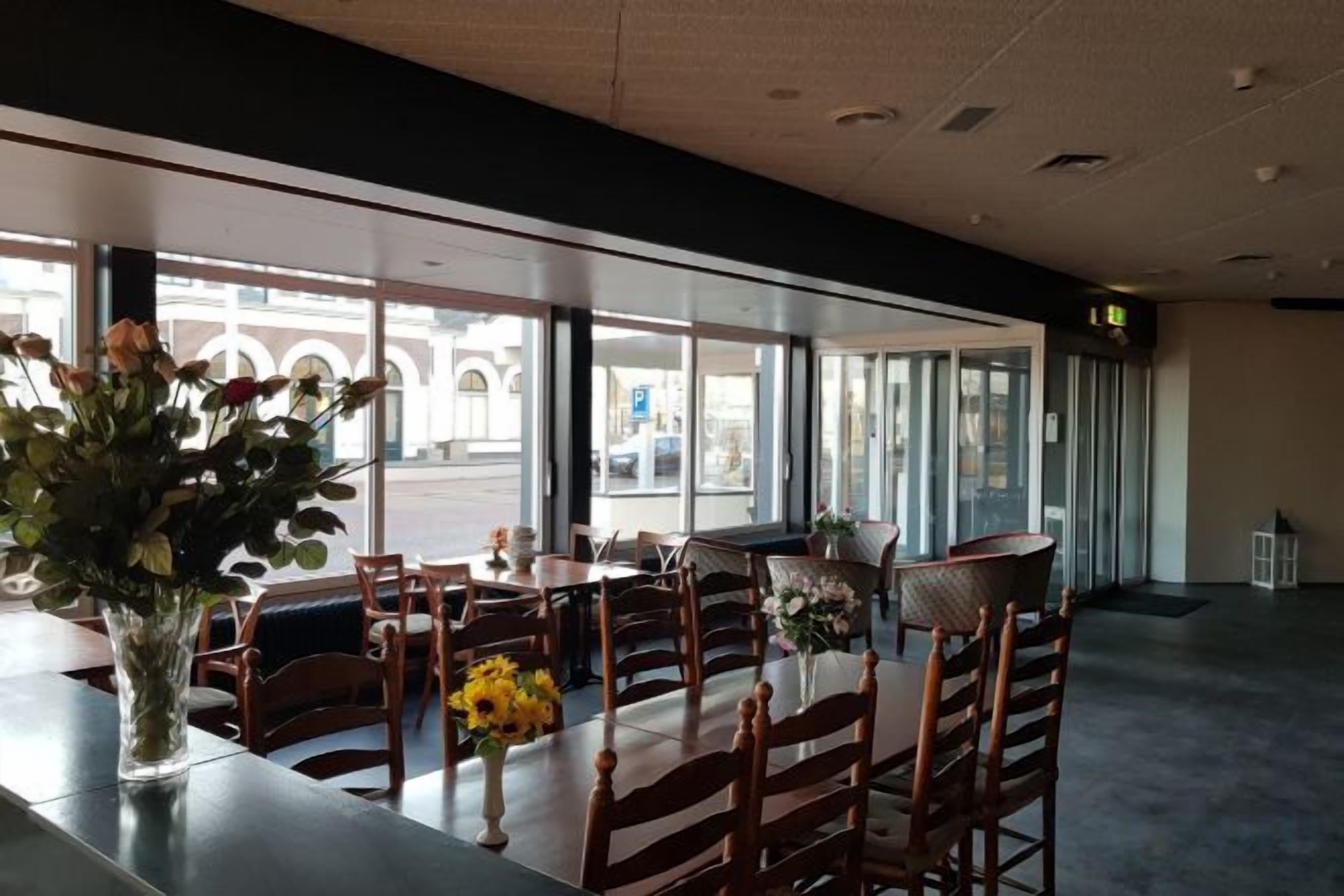 A restaurant with tables and chairs, large windows, and a view of the street.