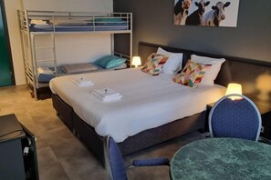 A bunk bed with a desk and chair, a bedside table with a lamp, and a wall with a cow picture.