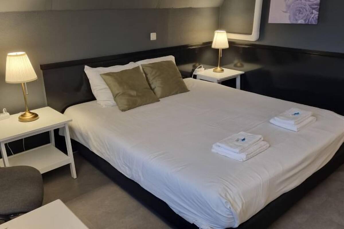 Un lit bien fait, avec du linge de lit blanc, deux lampes de chevet et des serviettes pliées posées sur le lit.