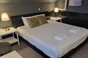 Una cama bien hecha con sábanas blancas, dos lámparas de noche y toallas dobladas sobre la cama.