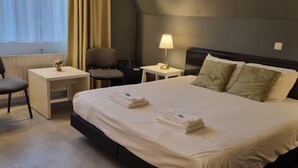 Quarto de hotel com cama, duas mesas de cabeceira, escrivaninha, cadeira e abajur.
