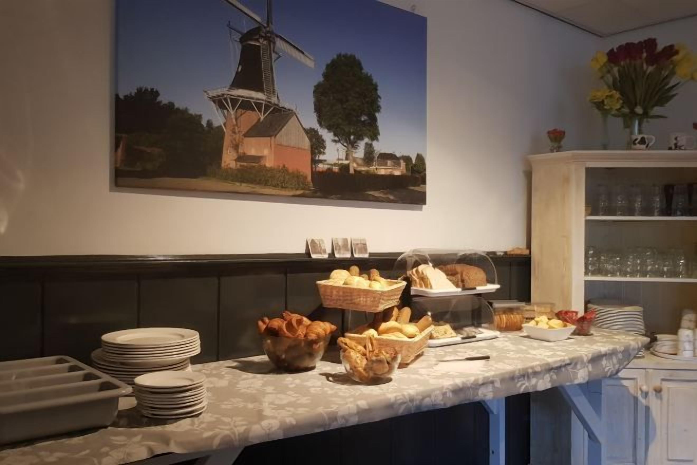Mesa de buffet con pan, frutas y un cuadro de un molino en la pared.