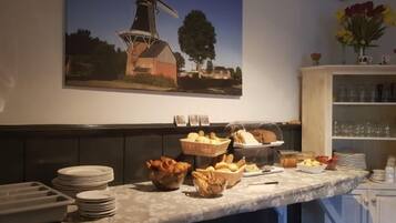 Mesa de buffet con pan, frutas y un cuadro de un molino en la pared.