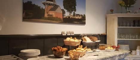 A buffet setup with various food items and a windmill painting on the wall.