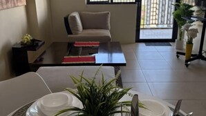 A dining area with a table set for four, a sofa, a coffee table, and a potted plant. - Cool Breeze-Serin West Tagaytay 1-bedrooom Condo (Tagaytay)