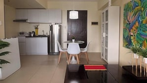 A modern kitchen with white cabinets, a stainless steel refrigerator, and a dining area with a round table and two chairs. - Cool Breeze-Serin West Tagaytay 1-bedrooom Condo (Tagaytay)