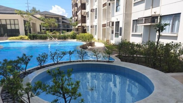 A swimming pool surrounded by a landscaped area with small trees and shrubs, adjacent to multi-story residential buildings. - Cool Breeze-Serin West Tagaytay 1-bedrooom Condo (Tagaytay)