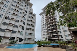Um edifício residencial com vários andares, varandas, piscina e áreas verdes ao redor.