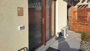 A building entrance with a sliding glass door, a small air conditioning unit, and a construction site visible through the window. - Kibou Apartment (Garbagnate Milanese)