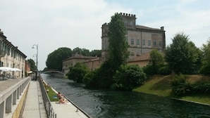 A river with a bridge, a castle-like building, and a walkway with people. - Kibou Apartment (Garbagnate Milanese)