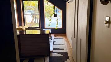 A narrow hallway with a wooden floor, a black and white rug, a wooden bench, and a window with a view of trees.
