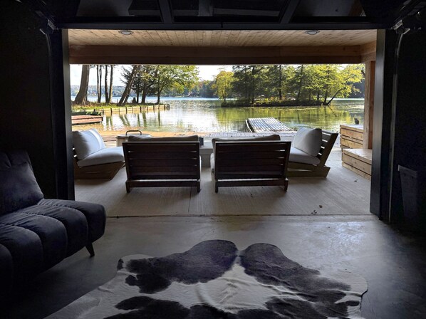 A room with a large window overlooking a lake, two wooden benches, a sofa, and a rug with a cowhide pattern.
