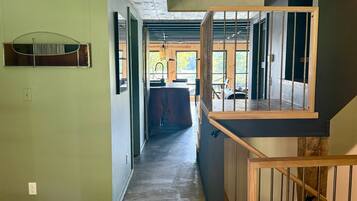 A modern interior with a wooden staircase, a kitchen area, and a view through a glass door.
