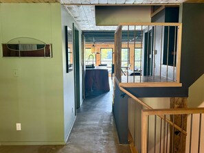 Um interior moderno com escada de madeira, área de cozinha e vista através de uma porta de vidro.
