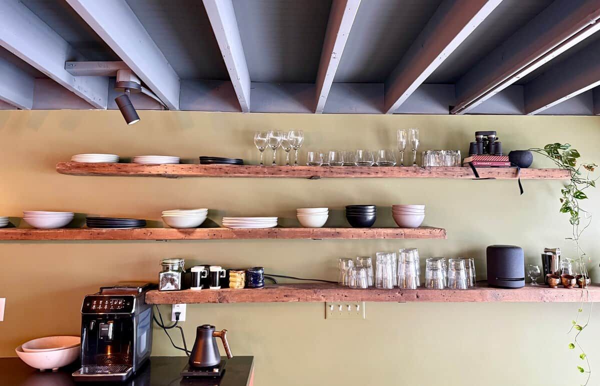 A kitchen with wooden shelves holding various dishes, glasses, and kitchen appliances.
