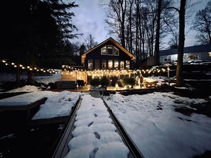 Uma cabana de madeira com varanda coberta, cercada por neve, e luzes de Natal.
