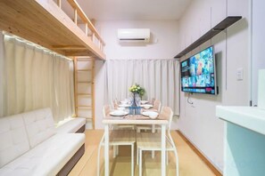 A compact living space with a sofa, a dining table with chairs, a TV mounted on the wall, and a window with curtains. - Kitaakabane • Diamond • Yu (Tokyo)