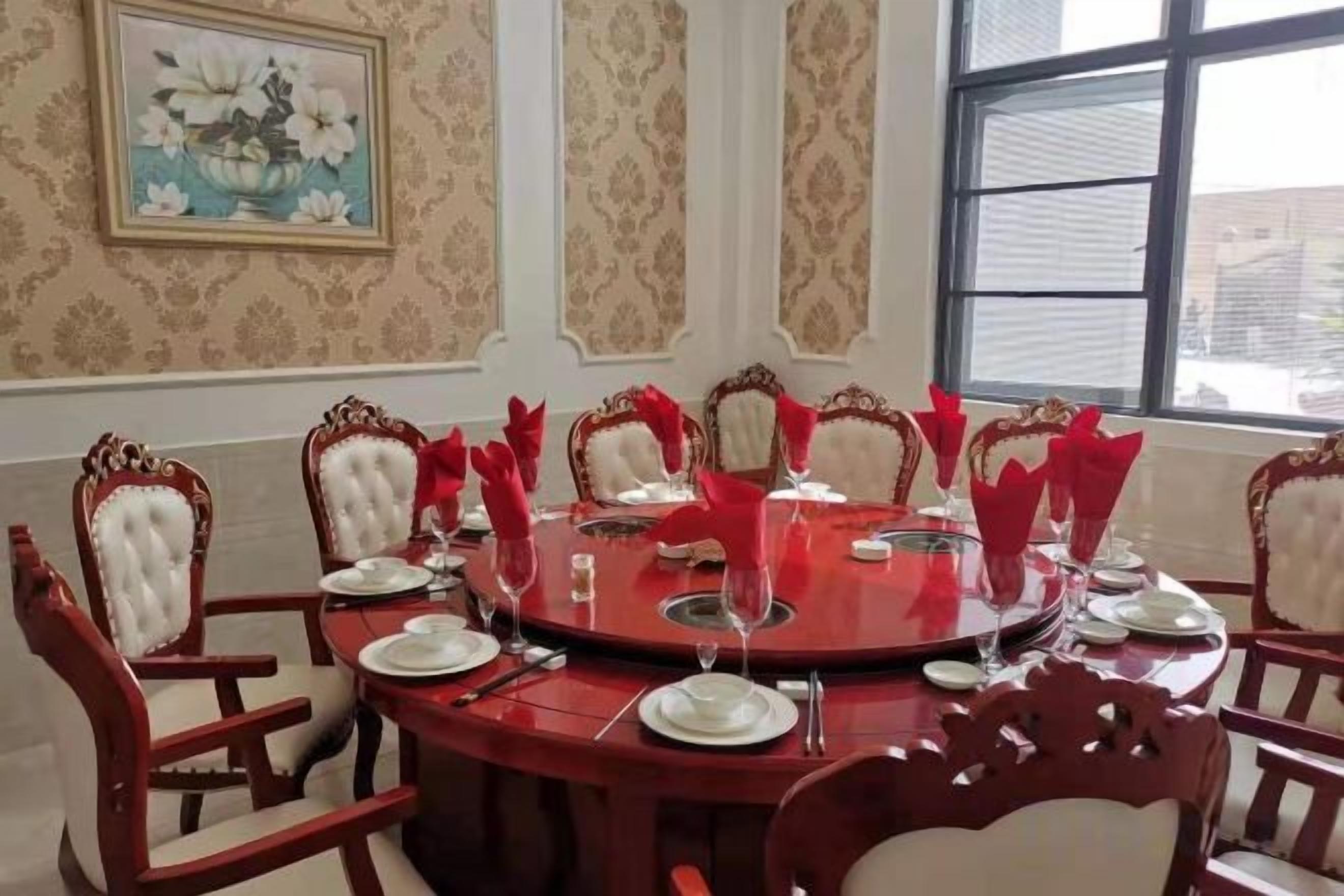 Comedor con una mesa redonda, servilletas rojas y sillas blancas.
