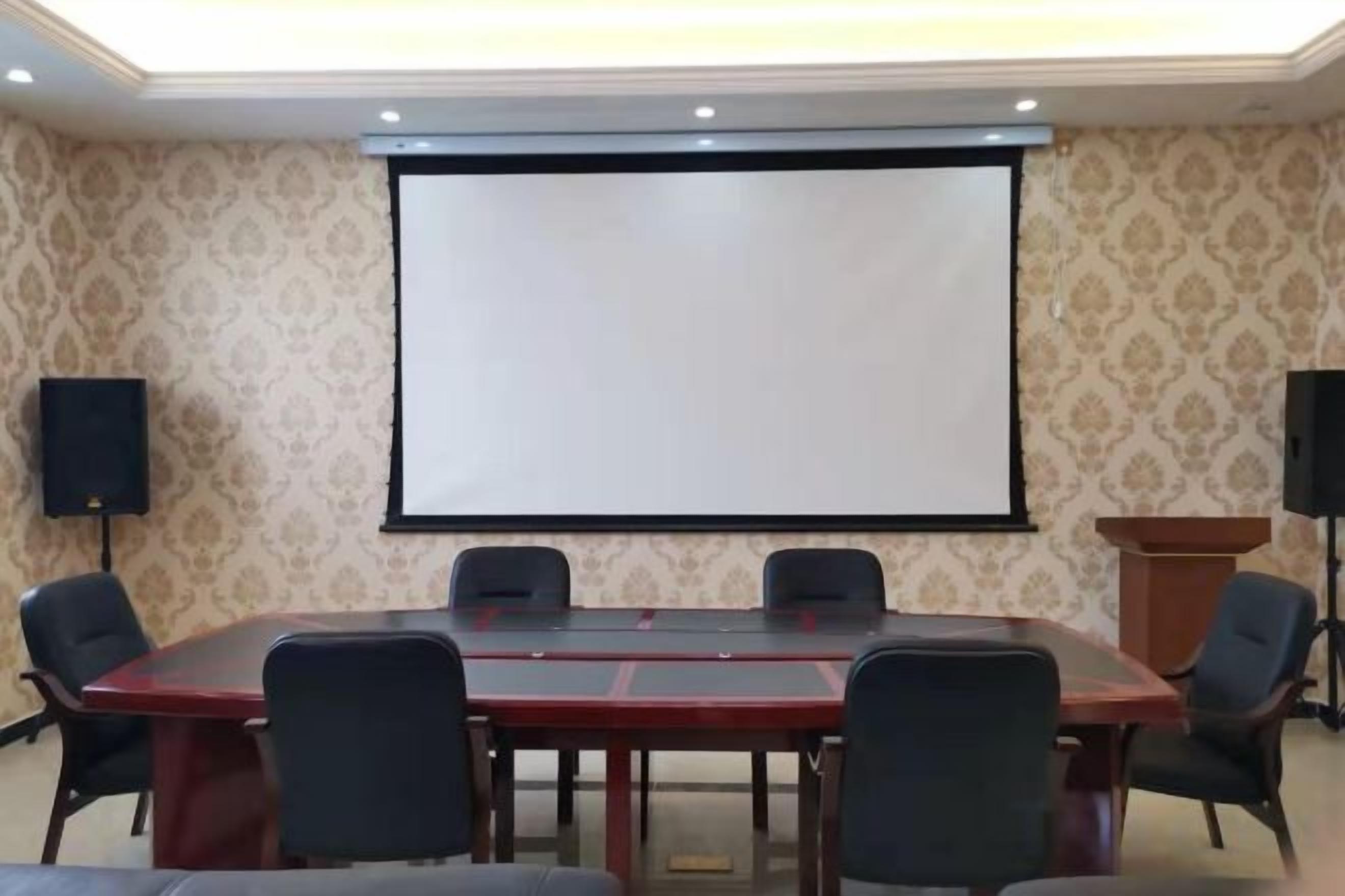 A conference room with a large table, chairs, a projector screen, and speakers.