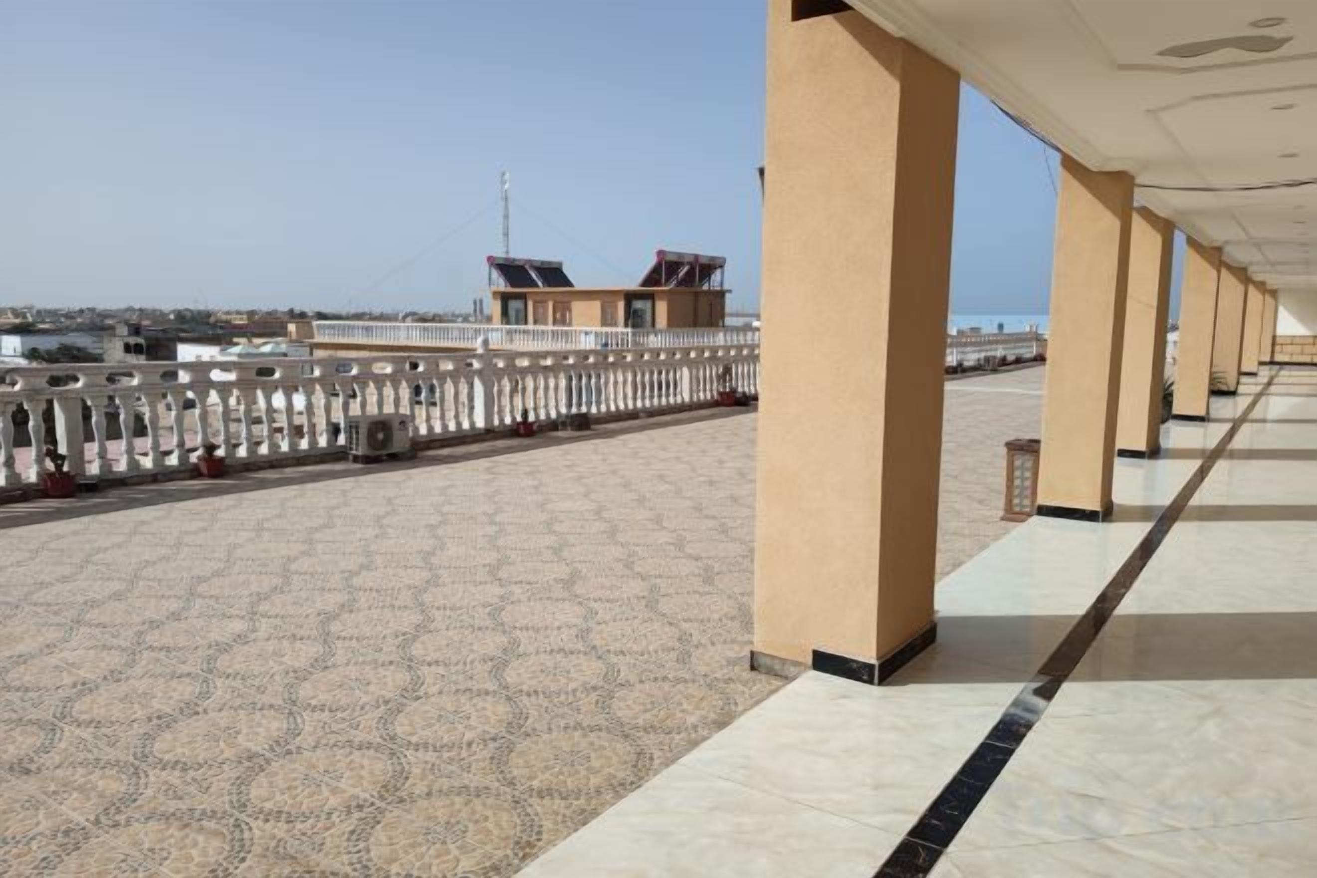 Un espacio al aire libre techado con piso estampado, columnas y barandilla con vista a un cuerpo de agua.
