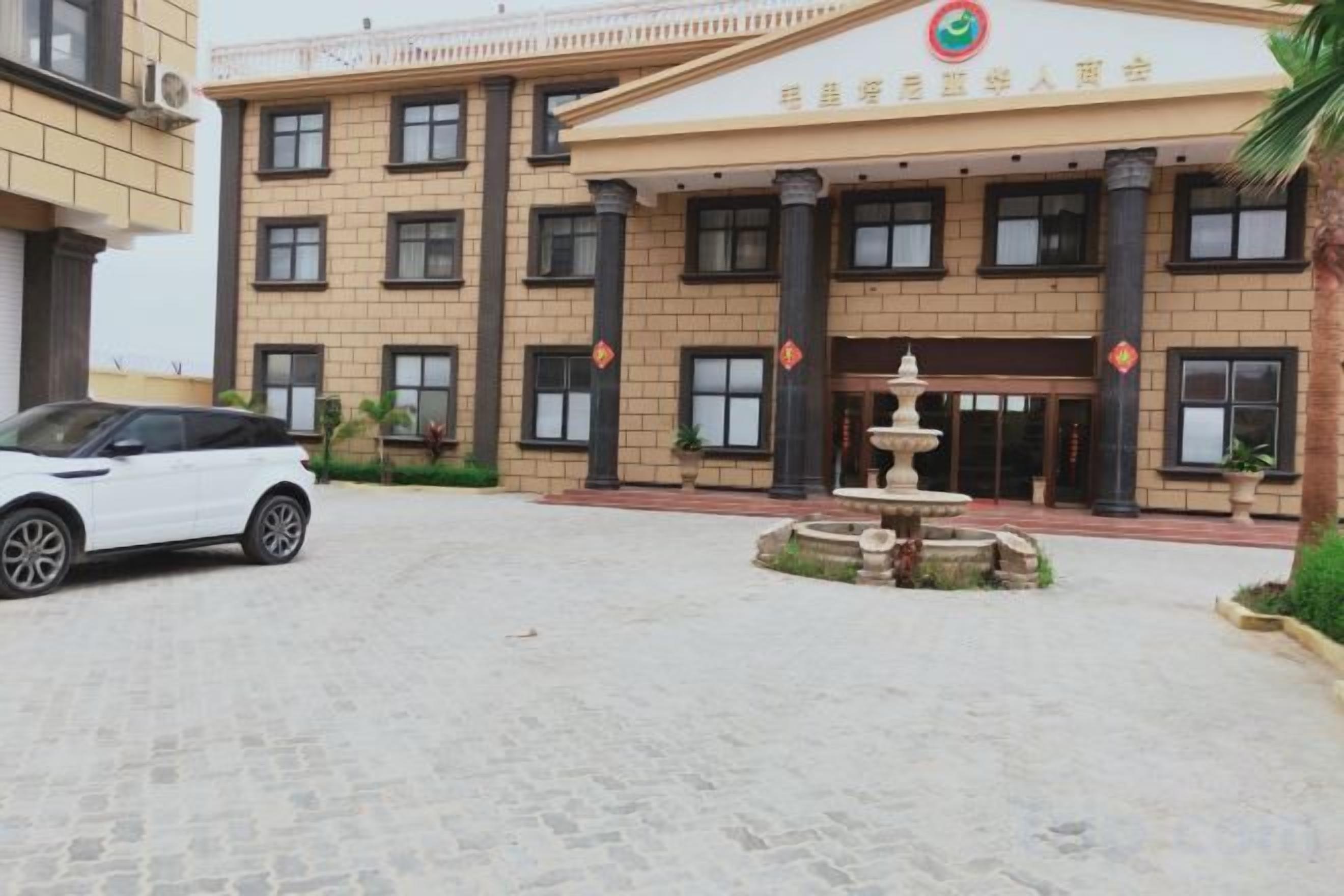 Un edificio con entrada central, una fuente y zona de estacionamiento.