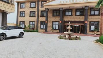 Un edificio con entrada central, una fuente y zona de estacionamiento.