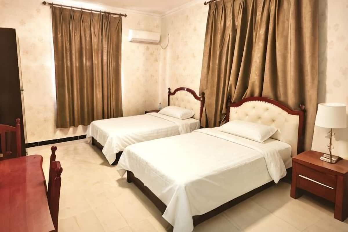 A hotel room with two beds, a wooden nightstand, a chair, and a desk.
