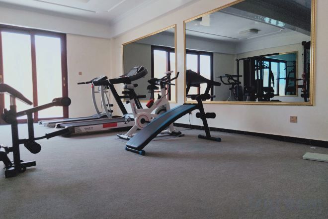 Un gimnasio con equipo de ejercicio, un espejo grande y suelo alfombrado.