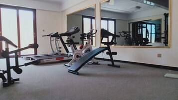 Un gimnasio con equipo de ejercicio, un espejo grande y suelo alfombrado.