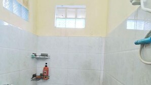 A bathroom with white tiles, a window, a shelf with toiletries, and a shower head. - Koh Rong Home Stay (Sihanoukville)